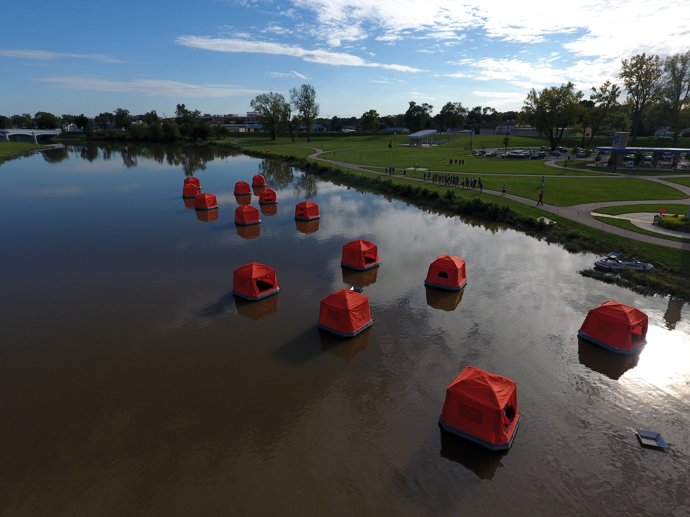 Aerial view of a dozen orange SmithFly Shoal Tents floating on a pond