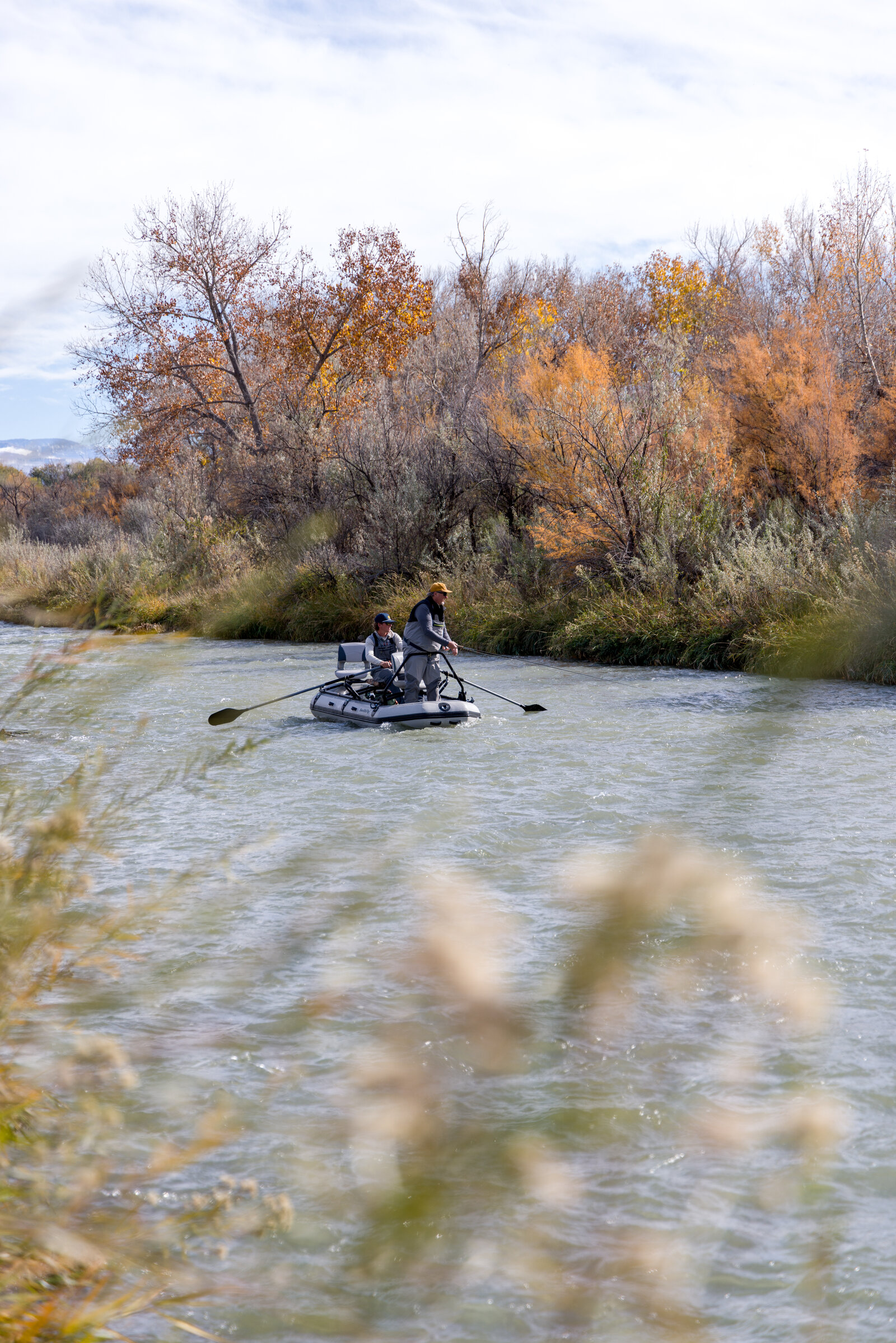 Two anglers fishing from a SmithFly raft along a tree-lined river