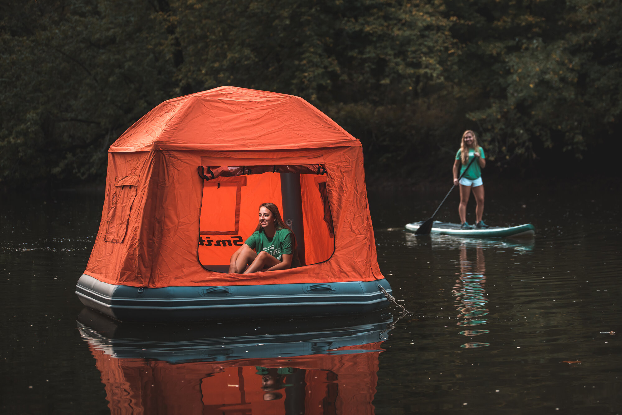 A person relaxing inside a SmithFly Shoal Tent while another paddleboards past